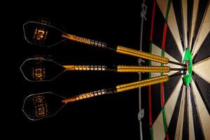 Sisal dartboard with three darts in a bullseye on a black background photo
