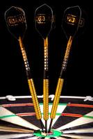 Sisal dartboard with three darts in a bullseye on a black background photo
