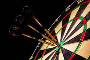 Sisal dartboard with three darts in a bullseye on a black background photo