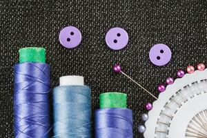 Sewing accessories spools of threads, needles, buttons, on the textured fabric surface photo