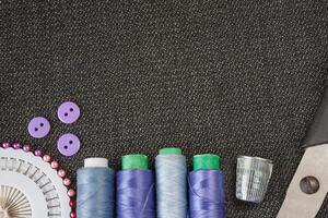 Sewing accessories spools of threads, needles, scissors, buttons on the textured fabric surface. Flat view with copy space photo