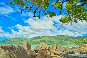 Anse royale beach, Mahe, blue sky turquoise water, low tide sunny day, white sandy beach and granite rock boulders, Seychelles mountain in the background photo