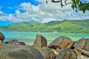 Anse royale beach, Mahe, blue sky turquoise water, low tide sunny day, white sandy beach and granite rock boulders, Seychelles mountain in the background photo