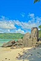 Anse royale beach, Mahe, blue sky turquoise water, low tide sunny day, white sandy beach and granite rock boulders, Seychelles mountain in the background photo