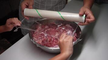 Young woman cooks raw marinated pork in a bowl and wrap it in clear plastic. video
