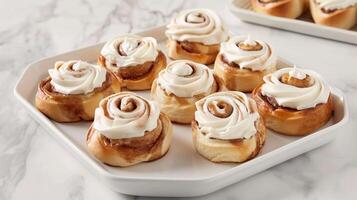 Homemade cinnamon rolls with cream cheese frosting, arranged on a white platter. photo