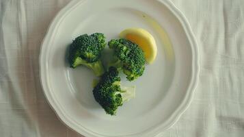 Steamed broccoli florets served with a wedge of lemon on a white plate. photo