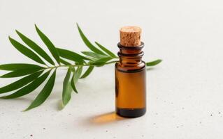 a bottle of essential oil with green leaves on a white surface with a brown cork stopper, photo
