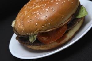 A meat burger on a white plate. A hamburger on a black background. Fast food. photo