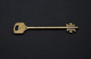 A copper key on a black background. The key to the front door. photo