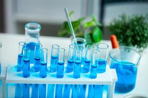 A row of blue test tubes sit on a white lab table. The tubes are filled with blue liquid and are arranged in a neat row. The table is also cluttered with other lab equipment, including a beaker photo