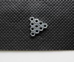 Triangle Made By Shiny Hex Nuts On A Black Plastic Sheet With White Stripe In The Lower Part Of Image photo