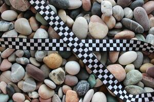 Racing Concept Design Stock Photo. Checkered Ribbon In Cross Form On A Colored Pebbles photo