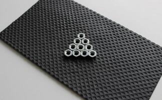 Steel Nuts In Play Button Shape On Black Rubberized Panel photo