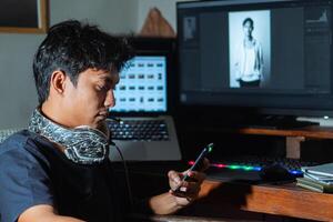 Young man using phone at desk with laptop and monitor photo