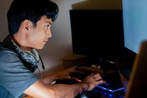 Young man typing on computer in dimly lit room photo