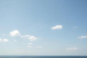 Clear blue sky with scattered clouds over calm ocean photo
