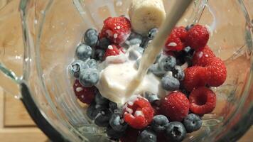 Milk is poured into a blender containing raspberries, blueberries and bananas. The milk splashes over the fruit as it is added. video