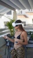 A woman is enjoying a virtual reality experience outdoors while wearing swimwear on a terrace video