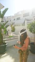A woman enjoys using her phone and VR headset on a sunny patio while wearing a sarong video