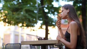 A woman is peacefully savoring ice cream at an outdoor cafe while wearing earbuds video
