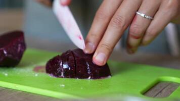 A closeup image depicting a person chopping fresh beets on a green cutting board video