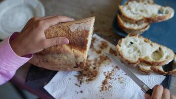 A child is cutting fresh bread on a table using a knife, creating crumbs in the process video
