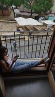 A woman sitting by a window, relaxing, and using her phone to text or browse the internet video