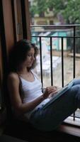 A woman enjoys a moment of peaceful reflection while reading by the window on a rainy day video