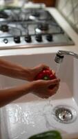 In a kitchen sink, someone is rinsing a red bell pepper under the faucet while cooking video