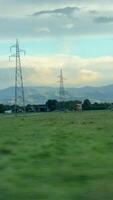 Picturesque scenery of power lines in a green field with mountains and clouds in the background video