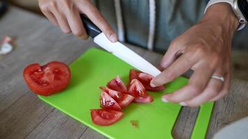 A closeup view of hands slicing fresh tomatoes on a green cutting board in a kitchen video