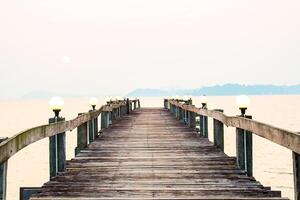 Serene Wooden Pier Extending into Calm Sea at Sunset with Soft Lighting and Distant Hills photo