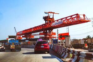 Large Red Construction Crane on Highway with Vehicles and Safety Barriers Under Clear Blue Sky photo