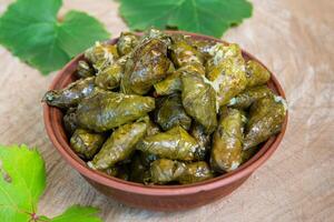 Dolma a stuffed grape leaves in a clay bowl on wooden background photo