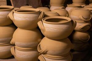 Freshly made clay mugs, pots and bowls drying up on wooden shelves in pottery workshop. Handmade ceramics manufacture. Different clay pots in workshop. photo