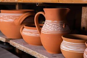 Freshly made clay mugs, pots and bowls drying up on wooden shelves in pottery workshop. Handmade ceramics manufacture. Different clay pots in workshop. photo