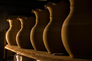 Freshly made clay mugs, pots and bowls drying up on wooden shelves in pottery workshop. Handmade ceramics manufacture. Different clay pots in workshop. photo