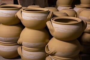 Freshly made clay mugs, pots and bowls drying up on wooden shelves in pottery workshop. Handmade ceramics manufacture. Different clay pots in workshop. photo