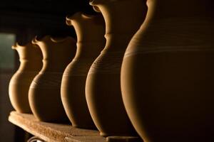Freshly made clay mugs, pots and bowls drying up on wooden shelves in pottery workshop. Handmade ceramics manufacture. Different clay pots in workshop. photo