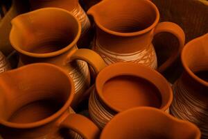 Freshly made clay mugs, pots and bowls drying up on wooden shelves in pottery workshop. Handmade ceramics manufacture. Different clay pots in workshop. photo