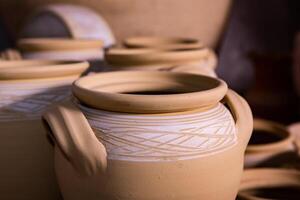 Freshly made clay mugs, pots and bowls drying up on wooden shelves in pottery workshop. Handmade ceramics manufacture. Different clay pots in workshop. photo