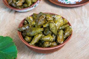 Dolma a stuffed grape leaves in a clay bowl on wooden background photo