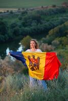 The beautiful lady holding the flag of the Republic of Moldova on a beautiful hill in nature. photo