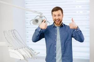 Portrait of happy patient near dental chair and shows a gesture with a thumb up class, good. Modern dentistry with the use of new technologies photo