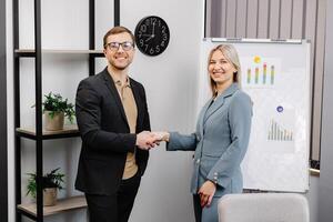 Smiling young female employee shake hand of male colleague make agreement or close deal at office meeting. Happy diverse business partners handshake get acquainted greeting at briefing. photo