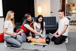Group of people learning how to make first aid heart compressions with dummies during the training indoors photo