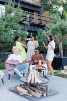 Multicultural group of people, man playing guitar and friends dancing, singing and having fun photo