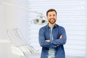 Confident male patient of stomatology standing in modern clinic. Man smiling at the camera crossing his arms in front of him photo