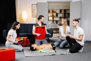 Young man instructor helping to make first aid heart compressions with dummy during the group training indoors photo
